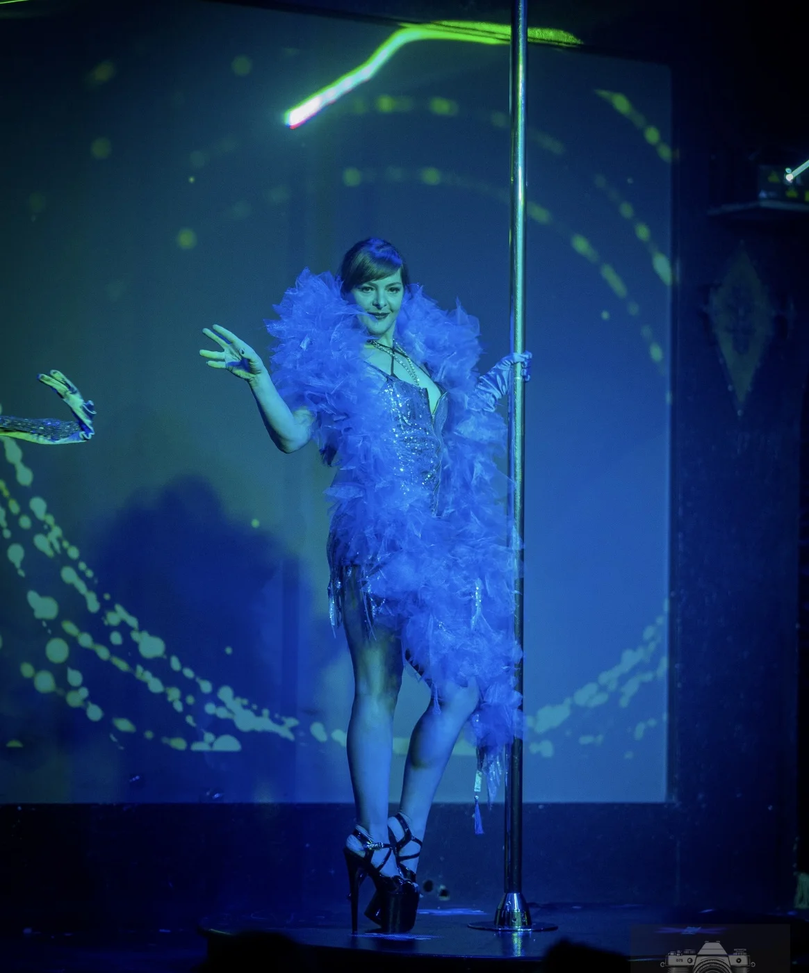 A performer with a blue feather boa on stage at the LUX Legacy 5 Year Anniversary Show in Tampa.