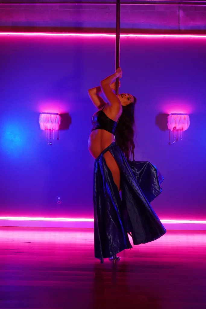 Polina Zueva reaching up the pole, pregnant, her long satin skirt sweeping behind her.