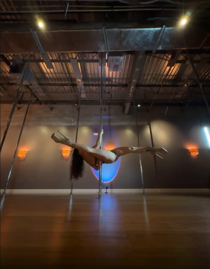 Polina Zueva horizontal on the pole in a wide split, from the handstand-and-split combo lesson.