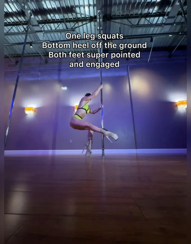 Polina Zueva in one-leg squats at the pole in platform heels, demonstrating toe box technique.